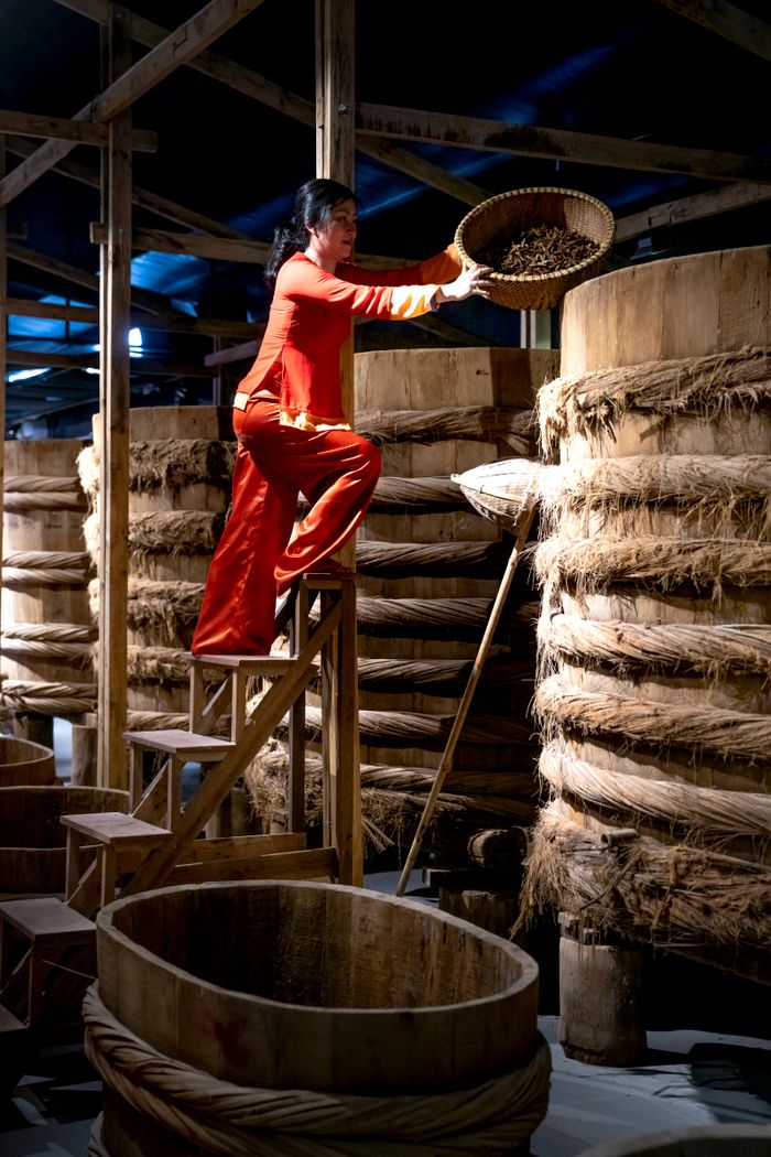 our-experience A woman in traditional attire manages barrels in an indoor warehouse setting.